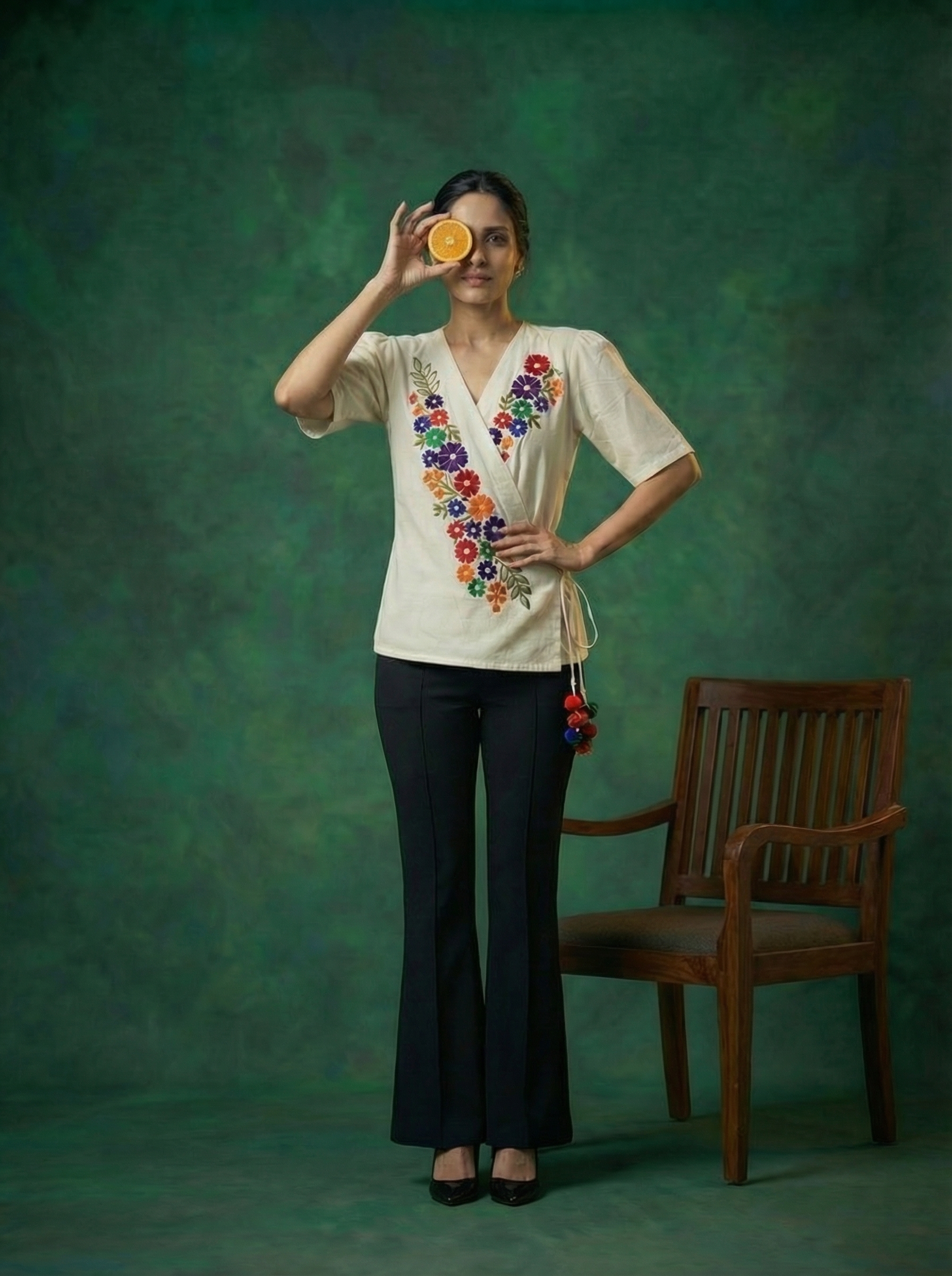 AI-generated fashion visual of a woman in a floral-embroidered top holding an orange slice